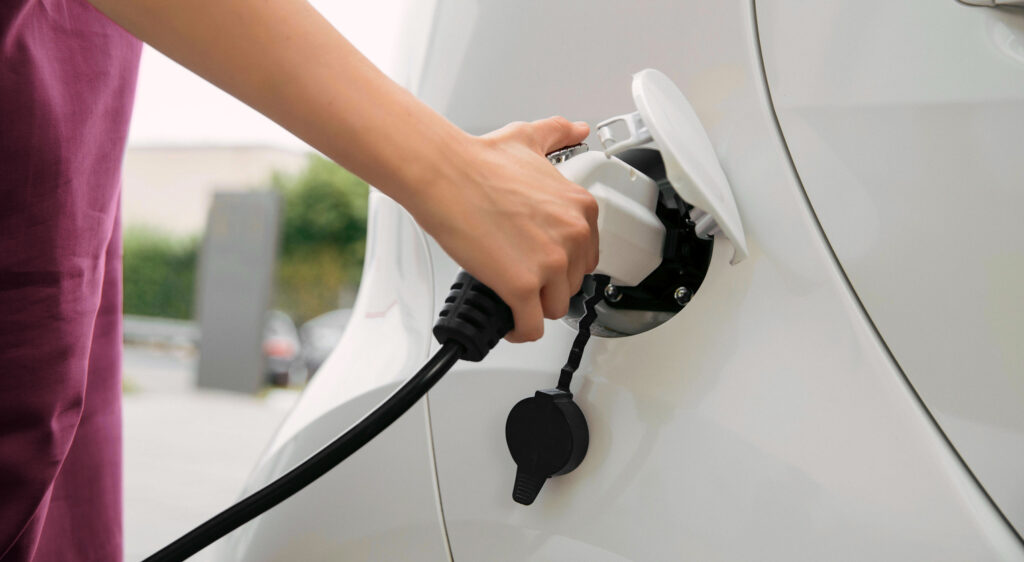foto van iemand die auto elektrisch oplaad.