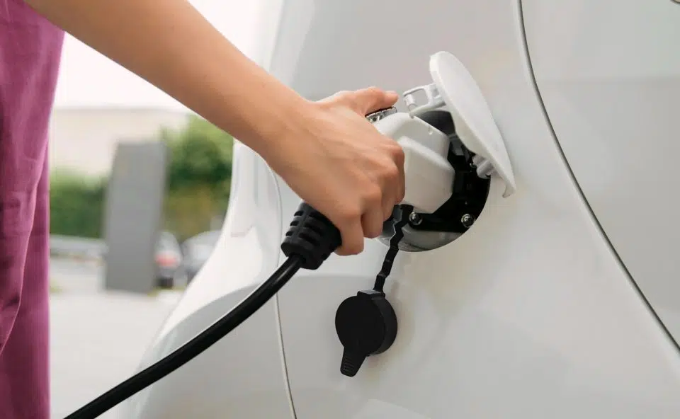 foto van iemand die auto elektrisch oplaad.