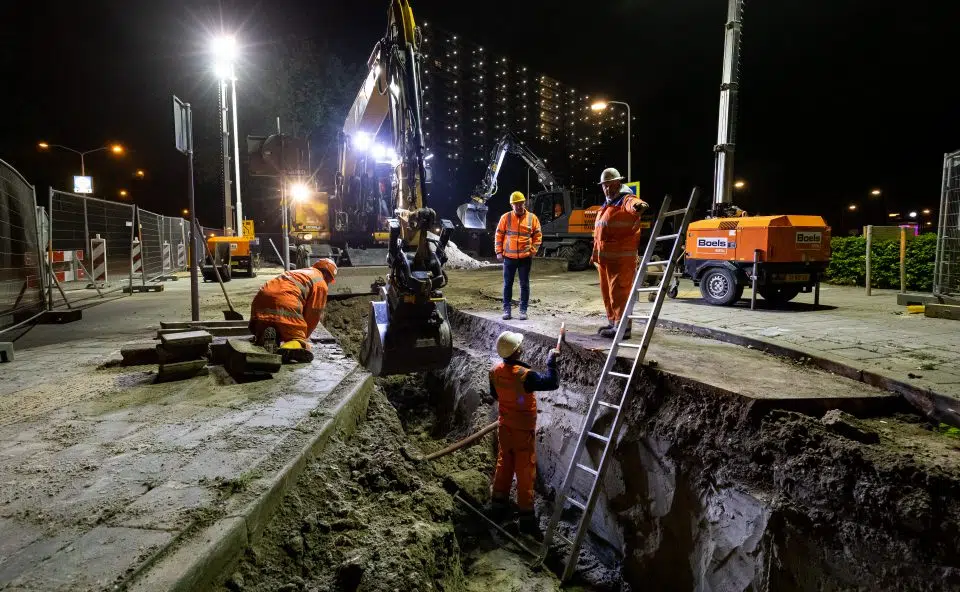 Nachtfoto van monteurs en graafmachines die warmteleidingen aanleggen in Zaanstad