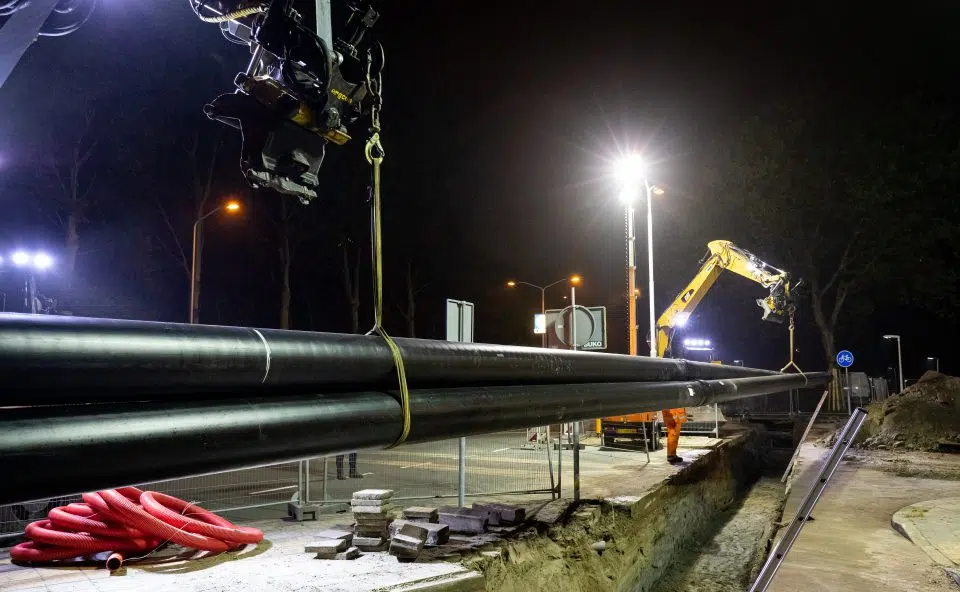 Nachtfoto van graafmachines die grote warmteleidingen plaatsen bij warmteaanleg in Zaanstad.