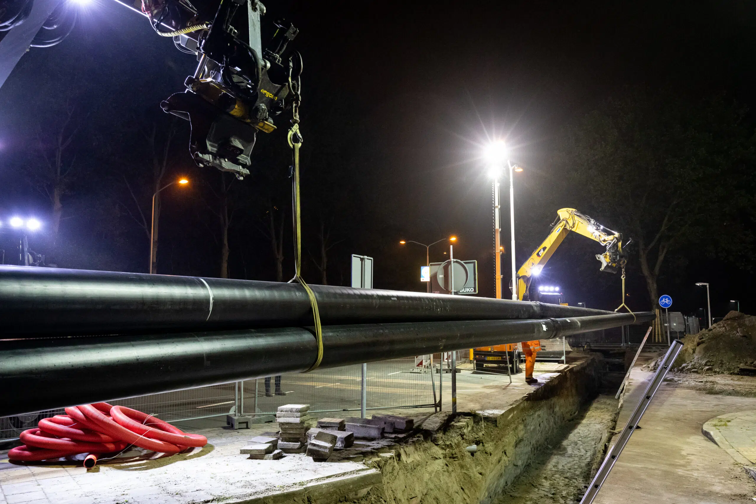 Nachtfoto van graafmachines die grote warmteleidingen plaatsen bij warmteaanleg in Zaanstad.