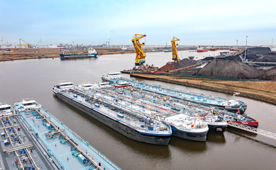 Overzicht van industrie in het Amsterdamse Havengebied met op de voorgrond vrachtschepen aan wal.