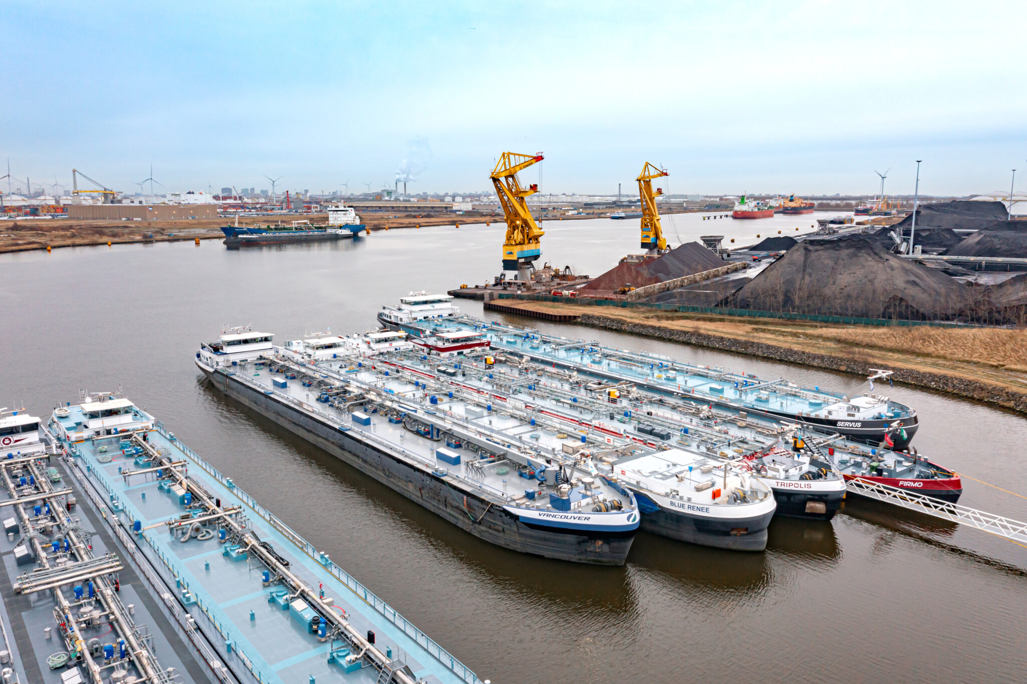 Overzicht van industrie in het Amsterdamse Havengebied met op de voorgrond vrachtschepen aan wal.